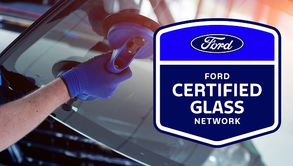 Hands of a person handling the glass shield of a vehicle and a badge with Ford Certified glass Network.